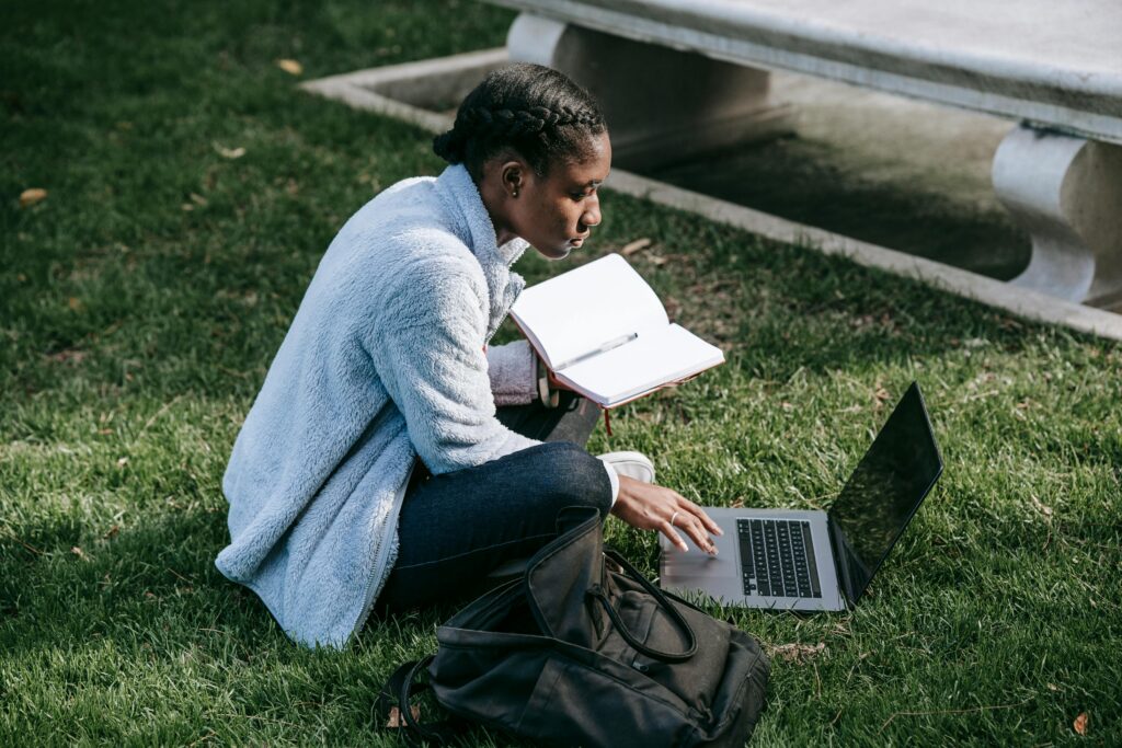 A college student studying her laptop while sitting on the grass.