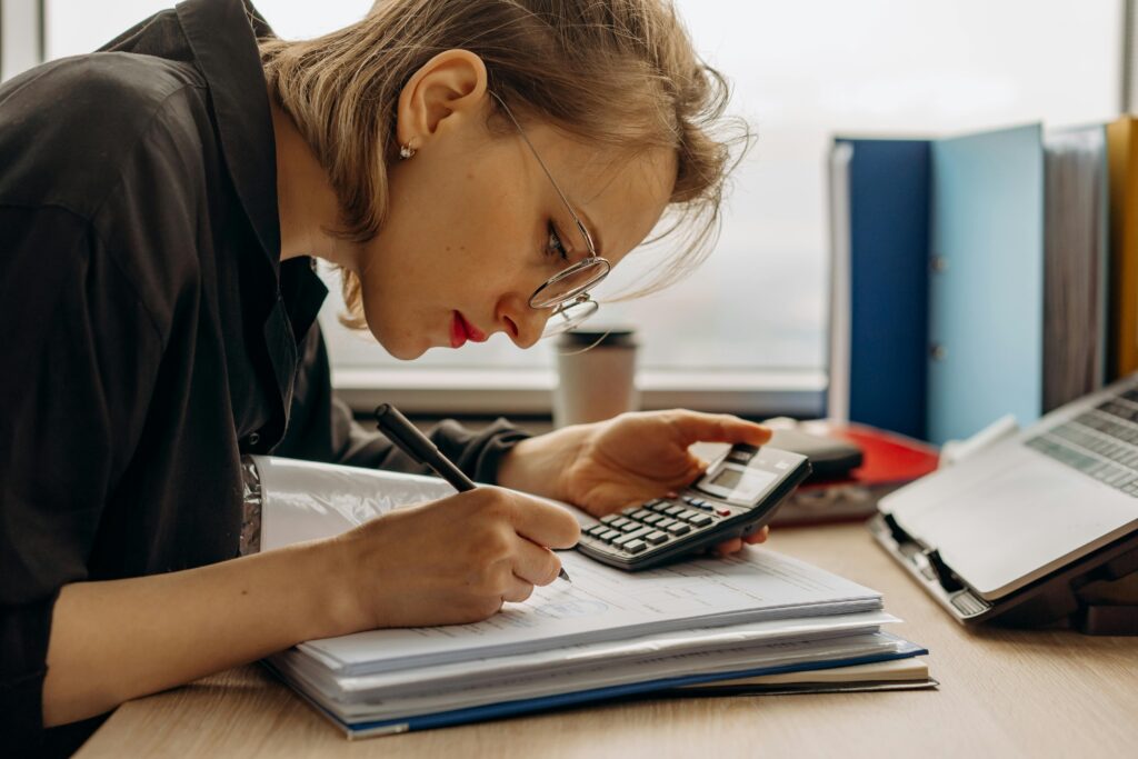 A woman doing calculations with a calculator, and writing down the answer. 