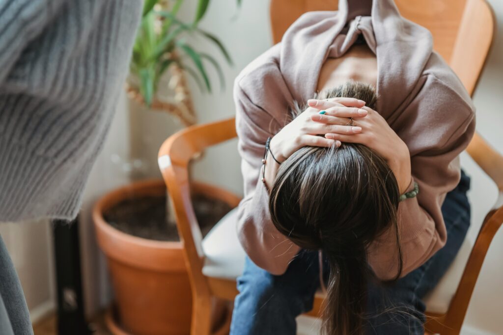 A woman slumped over in a chair, grasping her neck.
