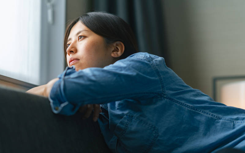 A young woman experiencing anxiety while looking out a window.