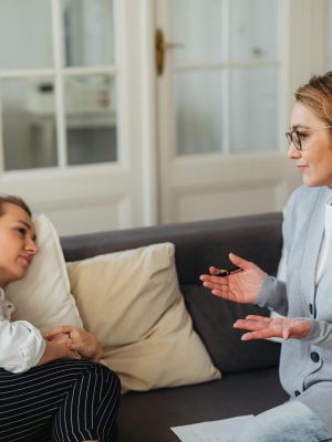 Two women talking while sitting on a couch.